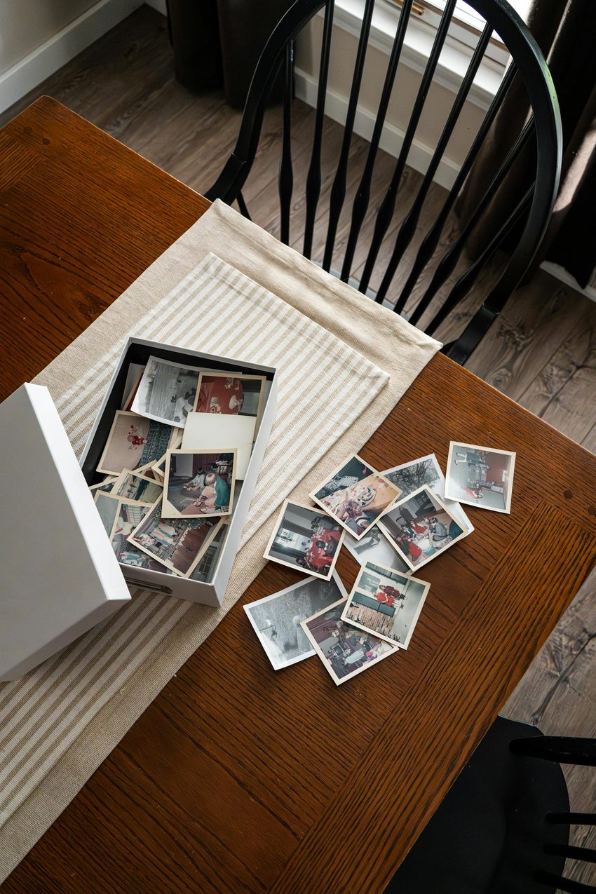 Collection of vintage family photographs scattered on a wooden table, some faded and worn, ready to be sorted and scanned for digital preservation