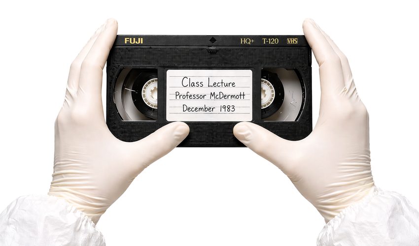 Gloved hands carefully handling a VHS cassette showing the magnetic tape through the clear window