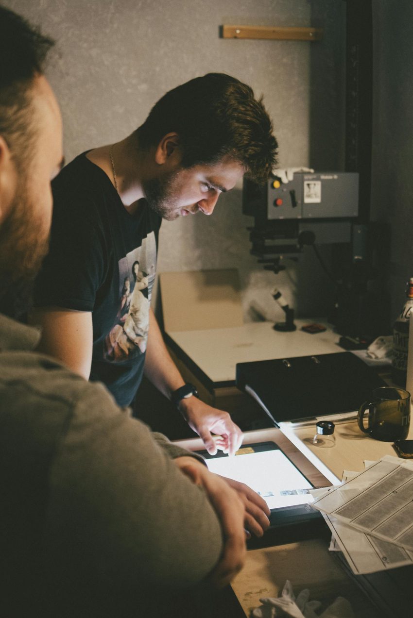 Technician examining film negatives on a lightbox in a darkroom environment demonstrating careful media handling and inspection process