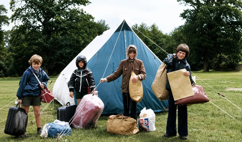 Four children with camping gear standing in front of family tent