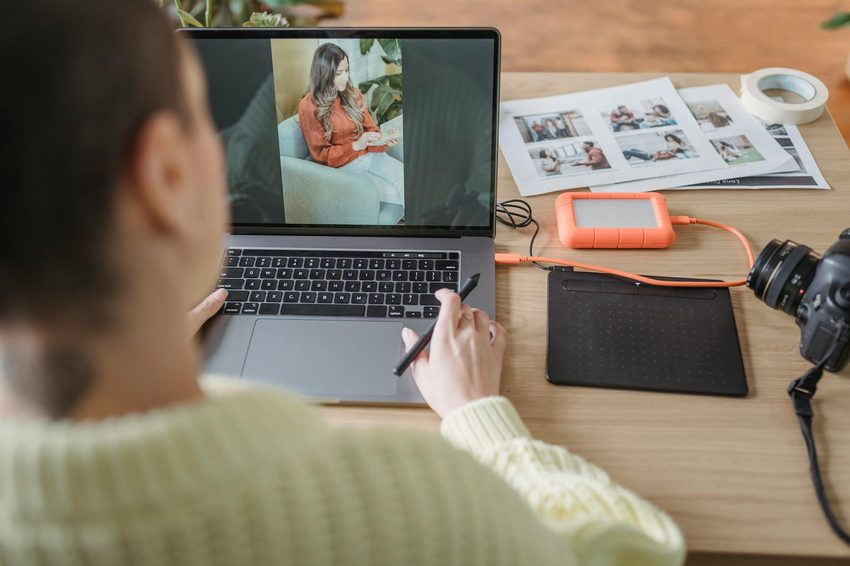 Photo retouching professional working on laptop with graphics tablet and printed reference photos showing the hands-on editing process