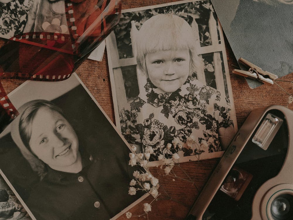 Old black-and-white family photographs laid on a wooden table alongside a vintage film strip and old camera