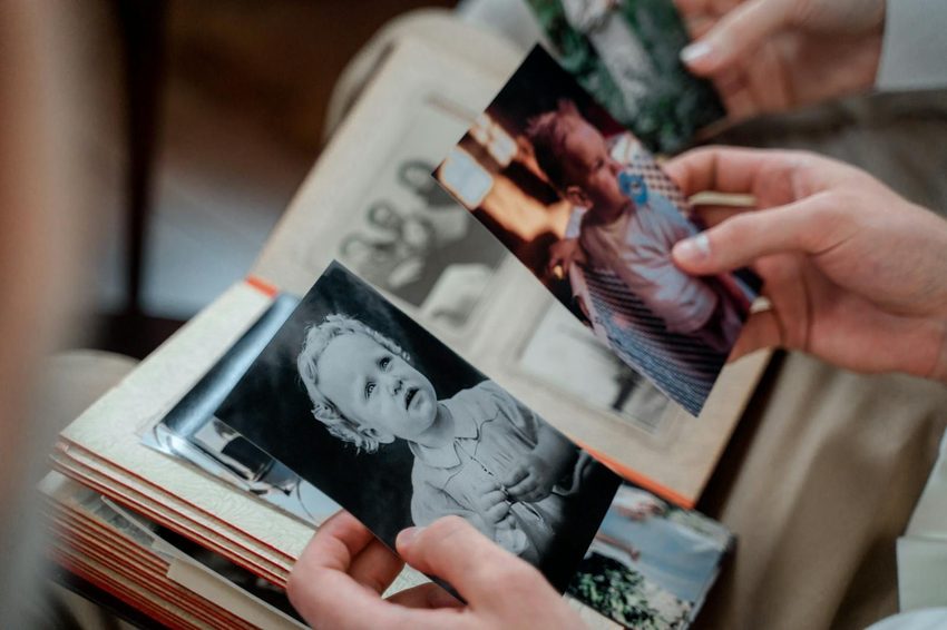 Hands carefully holding vintage black and white family photographs over a photo album preserving cherished family memories