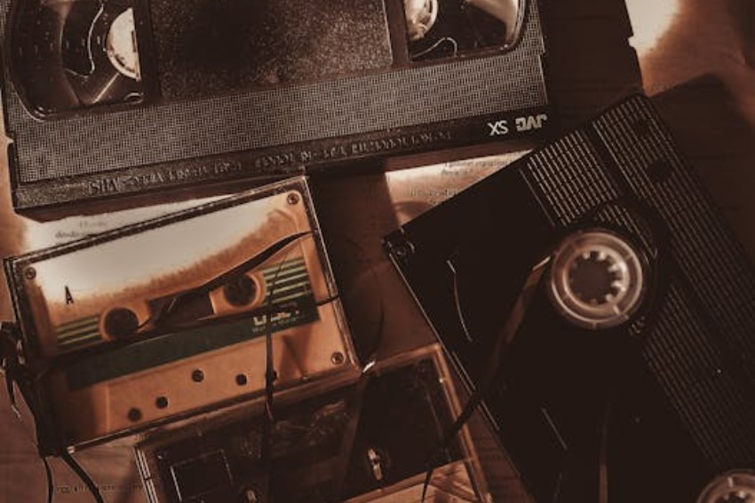 Stack of old VHS cassette tapes and audio cassettes on a wooden surface, sepia-toned, showing age and wear